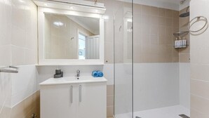 Ett modernt badrum med en dusch som är avskärmad med glasväggar, ett vitt handfat med spegel och en handdukshängare.