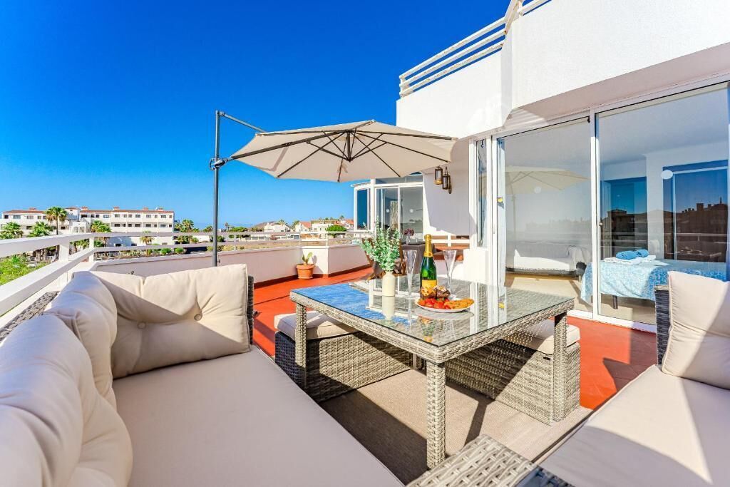 Een terras op het dak met een glazen tafel, zitplaatsen buiten en uitzicht over de stad.
