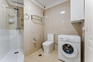 Ein kleines Badezimmer mit einer Duschkabine, einer Toilette und einer Waschmaschine mit Frontlader.