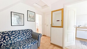 Een woonkamer met een sofa met patroon, een grote spiegel en uitzicht op een keuken.