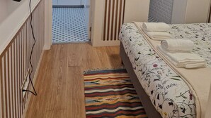 Habitació compacta amb un llit, televisió penjada a la paret, petita cuina i una catifa amb dibuixos.