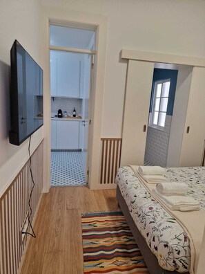 A compact room with a bed, a TV mounted on the wall, a kitchenette, and a patterned rug. - Charming one-bedroom apartment near Belém, Lisbon (Lisboa)