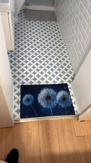 A hallway with patterned floor tiles, a doormat with a dandelion design, and a wooden floor. - Charming one-bedroom apartment near Belém, Lisbon (Lisboa)