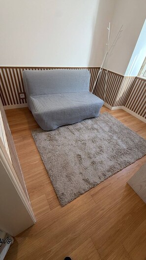 A room with a sofa and a rug on a wooden floor, a window, and a wall with vertical wooden slats. - Charming one-bedroom apartment near Belém, Lisbon (Lisboa)