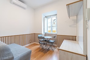 A small room with a wooden floor, a table with chairs, a bed, a window, and a telephone. - Charming one-bedroom apartment near Belém, Lisbon (Lisboa)