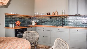 A compact kitchen with a tiled backsplash, wooden countertop, and a built-in oven. There are wicker chairs and a dining table with a patterned tablecloth. - Gorgeous home in Kivik with WiFi (Kivik)