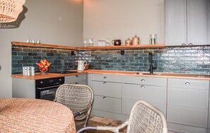 A compact kitchen with a tiled backsplash, wooden countertop, and a built-in oven. There are wicker chairs and a dining table with a patterned tablecloth. - Gorgeous home in Kivik with WiFi (Kivik)