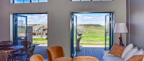 A modern interior with a sofa, chairs, a table, and a view of a vineyard through large windows.