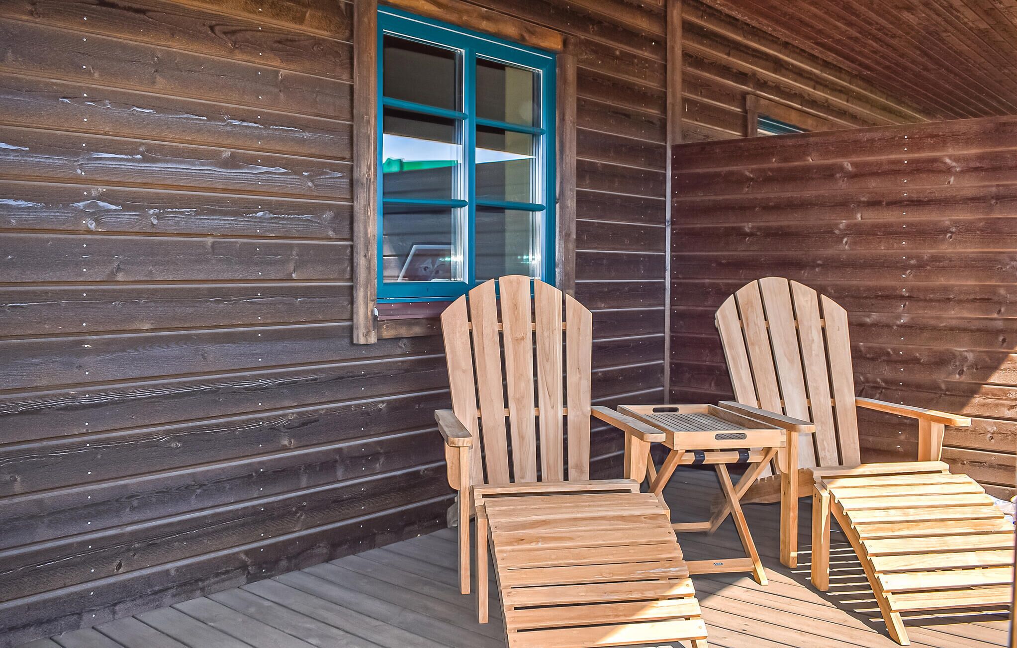 Een houten hutje met een veranda, twee Adirondack-stoelen en een tafel.