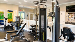 Ein Fitnessstudio mit unterschiedlichen Trainingsgeräten, darunter eine Hantelbank, Kurzhanteln und ein Ergometer.