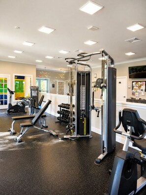 Ein Fitnessstudio mit unterschiedlichen Trainingsgeräten, darunter eine Hantelbank, Kurzhanteln und ein Ergometer.