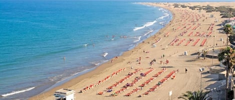 A beach with rows of sun loungers, a lifeguard tower, and a clear view of the ocean.