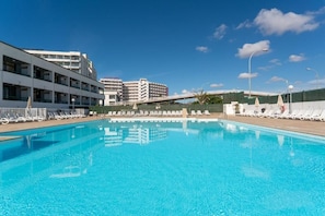 Una piscina con sillas de descanso y un edificio moderno al fondo.