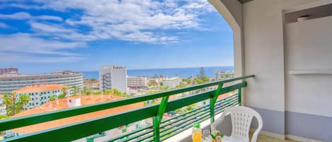 Un balcón con una mesa dispuesta para el desayuno, vista del paisaje urbano y cielo despejado.