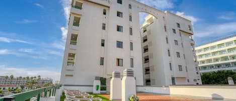 A modern hotel with a prominent archway, multiple balconies, and a rooftop area with sun loungers.