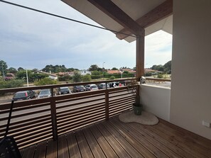 Ein Balkon mit Holzboden und Geländer, der auf einen Parkplatz und Wohnhäuser blickt.