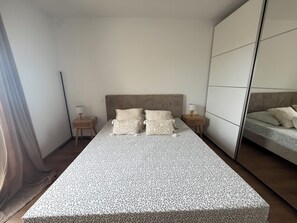 Ein ordentlich bezogenes Bett mit gemusterten Betttextilien, zwei Nachttische mit Lampen und ein großer Spiegel an der Wand.