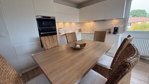 Una cocina moderna con armarios blancos, una mesa de comedor de madera, sillas de mimbre y un horno empotrado.