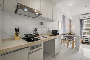 A modern kitchen with a central island, built-in appliances, and a dining area with bar stools. - Moris by Kozystay - Alam Sutera (Tangerang)
