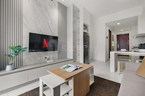 Cocina moderna con televisor integrado, comedor con taburetes y una sala de estar con sofá.