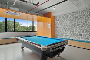 Een pooltafel in een ruimte met grote ramen, een behangwand en zichtbare leidingen aan het plafond.