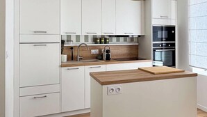 Eine moderne Küche mit weißen Schränken, einer Kücheninsel mit Holzplatte, einer schwarzen Pendelleuchte und eingebauten Geräten.