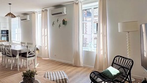 Ein modernes Wohnzimmer mit Essbereich, Holzboden und einem großen Fenster mit Vorhängen.