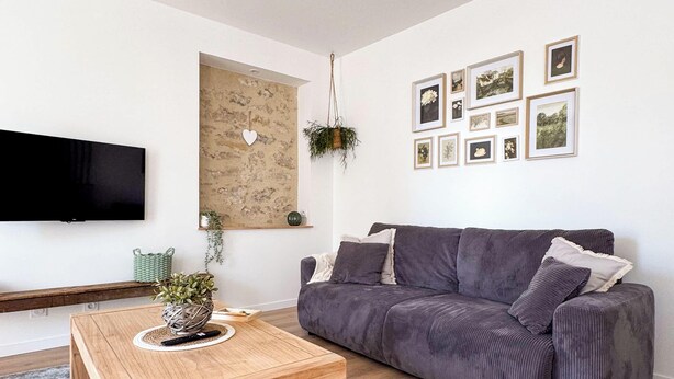 Ein modernes Wohnzimmer mit grauem Sofa, Couchtisch aus Holz, Flachbildfernseher und einem an der Wand befestigten Bilderrahmen.