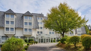 Ett hotell med flera våningar, en central entré och omgivet av grönska samt en asfalterad uppfart.