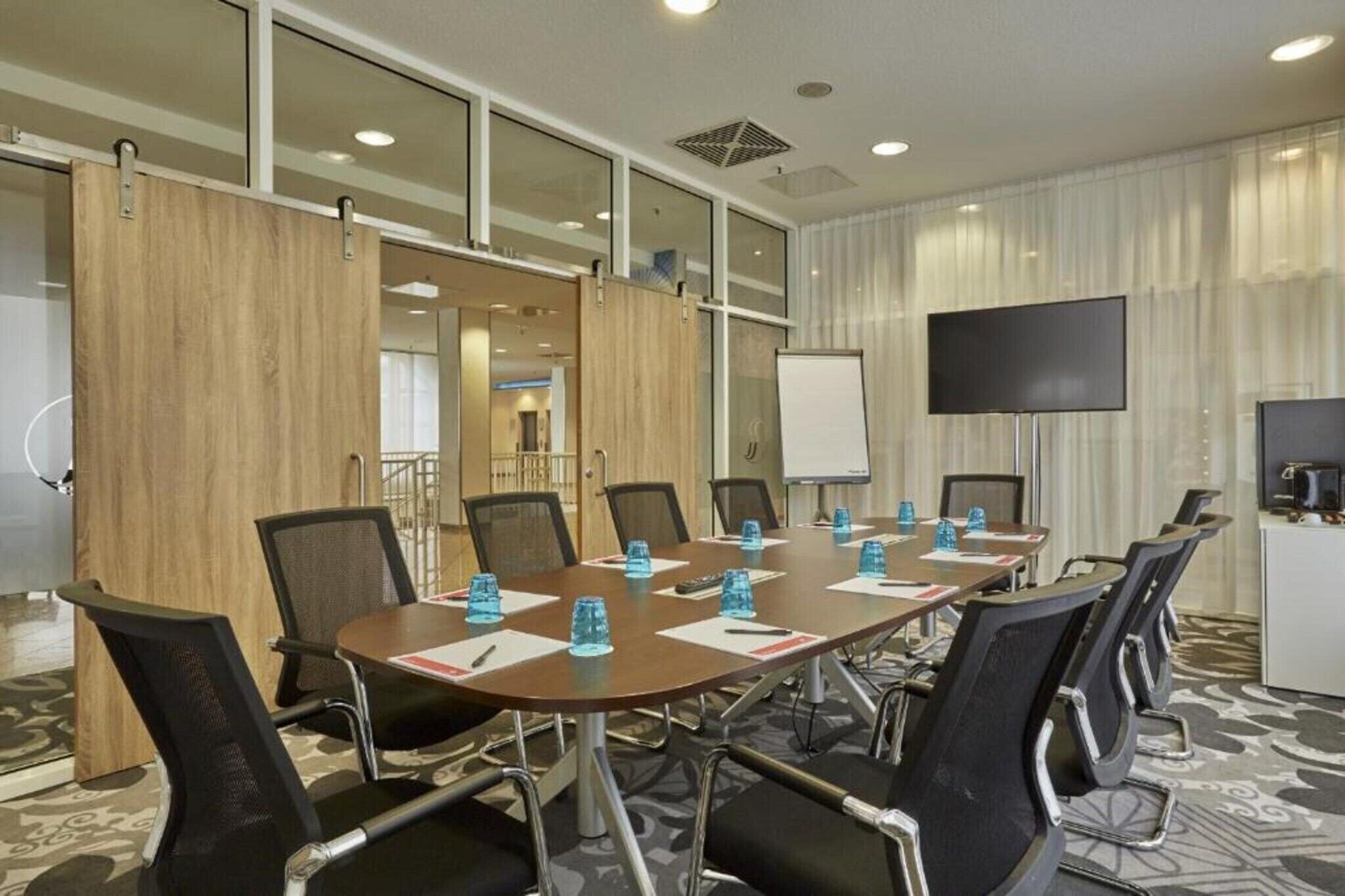 Un salón de conferencias con una larga mesa, sillas, una pizarra y una televisión.