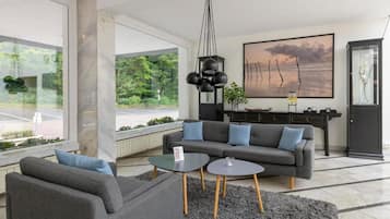 A modern living room with a grey sofa, two side tables, and a large window offering a view of greenery.