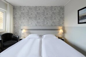 A hotel room with two beds, a headboard, two bedside lamps, a chair, and a window.