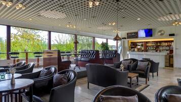 A spacious indoor area with leather seating, a bar area, and large windows offering a view of greenery.