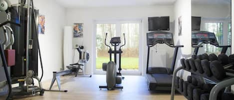A home gym with a treadmill, elliptical, stationary bike, and weight bench.