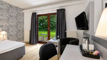 A hotel room with a bed, a desk with a coffee maker, a TV, and a view of the outdoors.