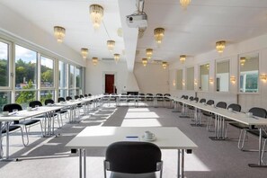 A conference room with long tables, chairs, a projector, and chandeliers.
