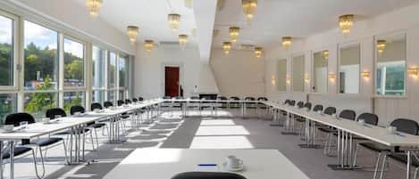 A conference room with long tables, chairs, a projector, and chandeliers.
