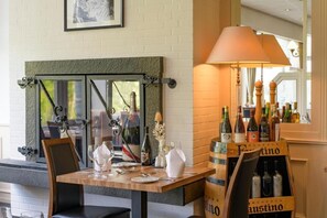 A dining area with a table set for two, a fireplace, and a wine rack with bottles. - Sunday Hotel des Norden deluxe double room (Harrislee)
