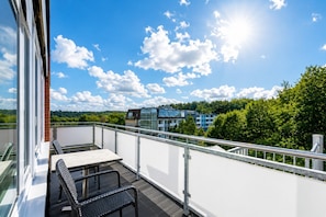 A balcony with a table and chairs, overlooking a cityscape with buildings and greenery.