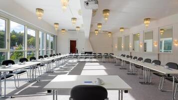 Une salle de conférence équipée de longues tables, de chaises, d’un projecteur et de lustres.