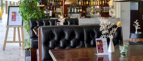 A bar area with black leather seating, a wooden table, a hanging pendant light, and a sign for 'Just Coffee.'