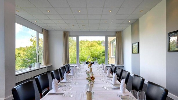 Ein Konferenzraum mit langem Tisch, gedeckt für eine Besprechung, großen Fenstern mit Blick auf Grünflächen und einer Decke mit Einbaustrahlern.