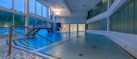 An indoor swimming pool with a tiled floor, a staircase, and large windows.