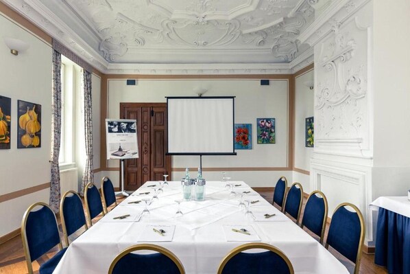 A conference room with a long table, blue chairs, a projector screen, and framed artwork on the walls.