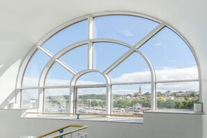 Ett rum med ett stort, välvt fönster som ger utsikt över en småbåtshamn och byggnader.