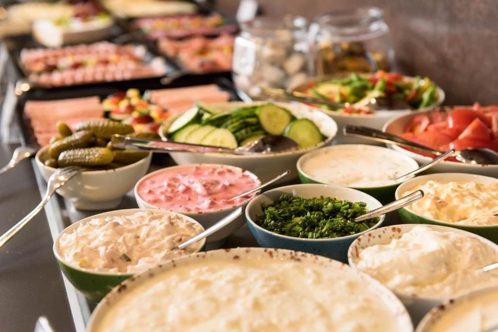 A buffet with various dishes including salads, dips, and a variety of meats.