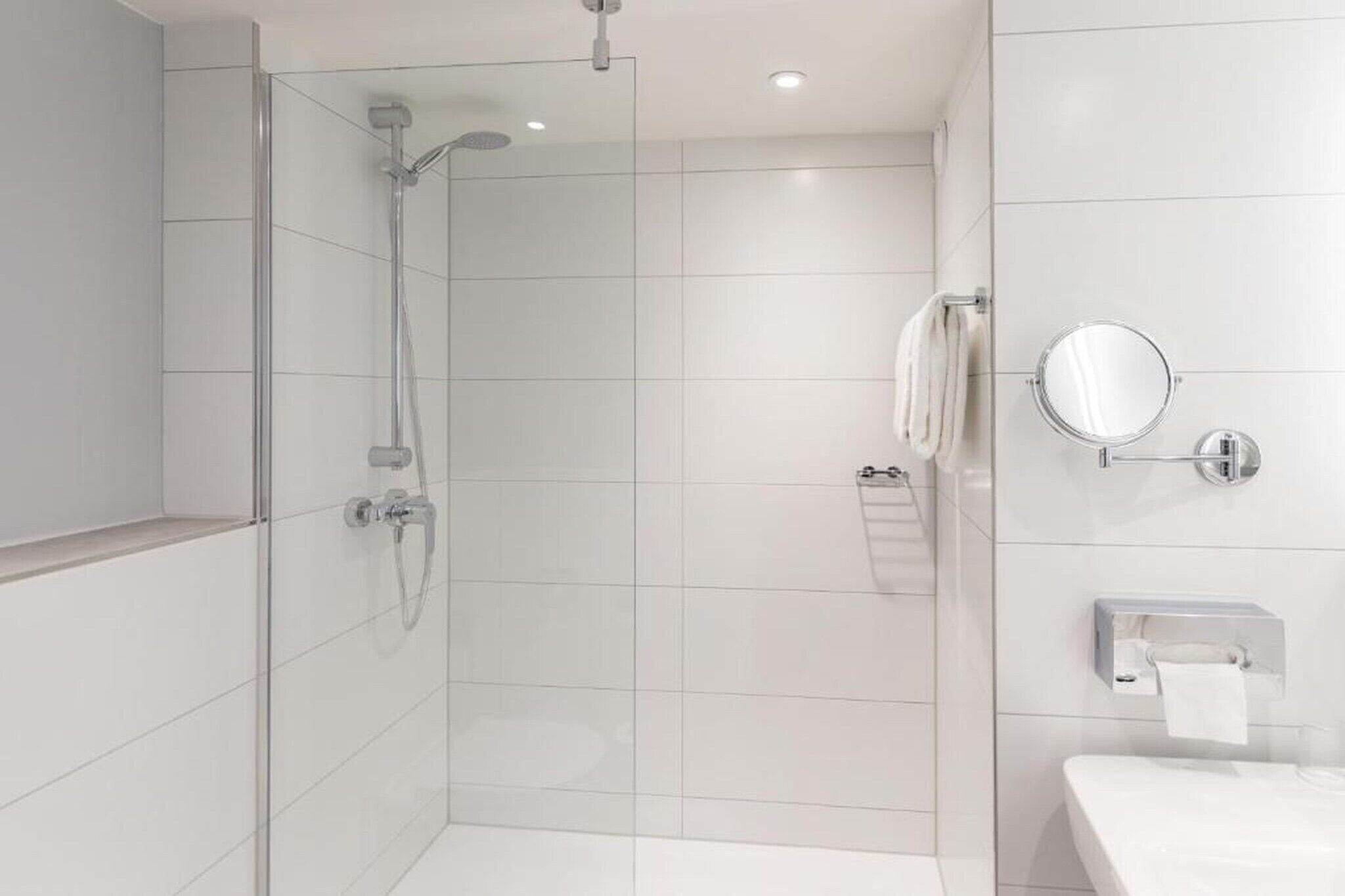 Ein modernes Badezimmer mit einer Duschkabine aus Glas, einem weißen Waschbecken, einem Spiegel und einem Handtuchhalter.