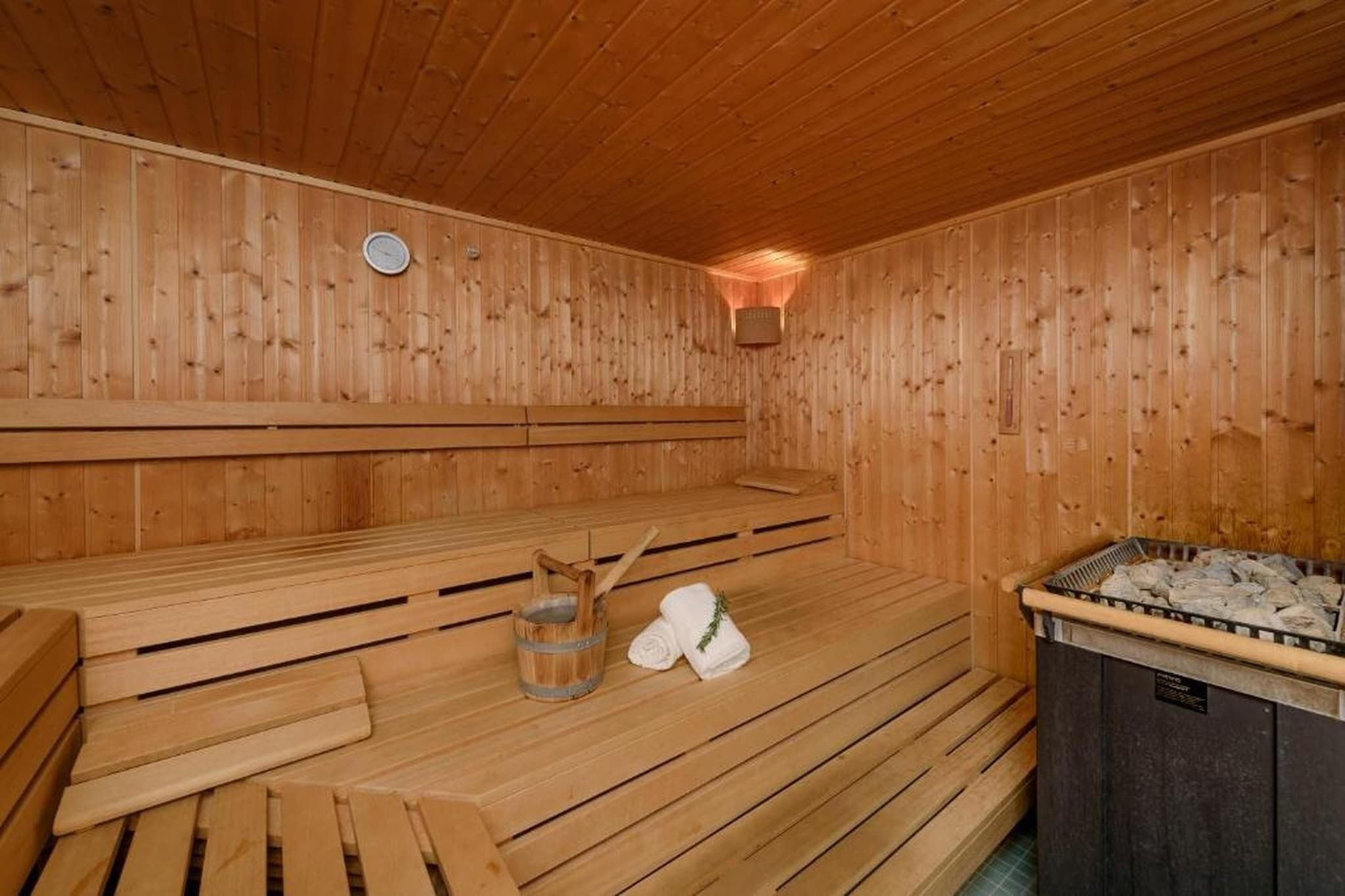 Eine Sauna mit Holzbänken, einem Eimer, Handtüchern und einem mit Steinen gefüllten Behälter.