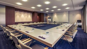 Een vergaderzaal met een lange tafel, stoelen, een projectiescherm en een whiteboard.