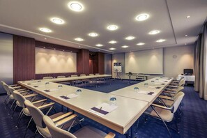 Une salle de conférence équipée d’une longue table, de chaises, d’un écran de projection et d’un tableau mobile.